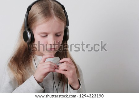 Little blond girl with headphones  listening music on a grey background