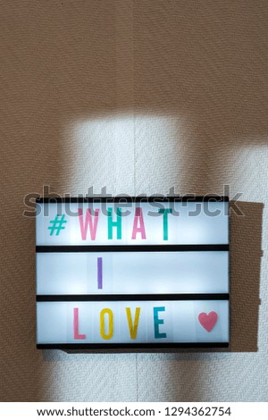 Message What I Love on illuminated board. Love affirmation concept with text. Daylight from window. Room interior. Coloured letters What I Love and hashtag on white wallpaper wall.