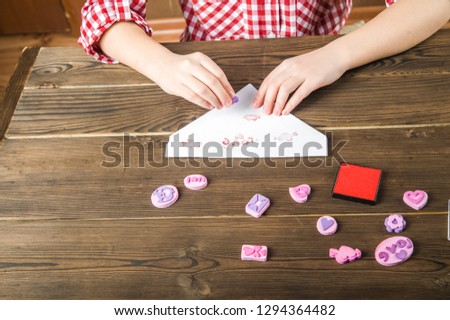 The girl writes a love letter for Valentine's Day. The girl writes a letter of thanks to mom and dad. Stamps and a letter on a textural wooden table. Diy love message