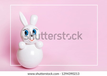 White toy on a pink background, space for text, space for design, a toy Bunny, a roly-poly.