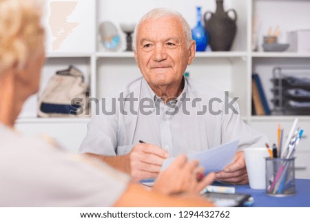 Smiling senior man sitting at home table discussing with wife their bills
