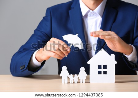 Male insurance agent covering paper family and home with umbrella cutout at table, closeup Royalty-Free Stock Photo #1294437085