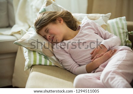 Child lying on sofa in the living room with stomach pain. Hands on belly. Little girl suffering Royalty-Free Stock Photo #1294511005