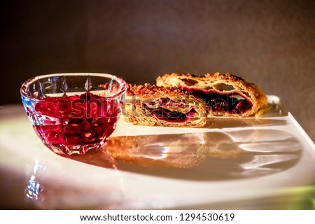 Two sliced peaces of the the pie with red jam inside covered by sugar  and  saucer with raspberry in gray blur as background. This picture made by middle format camera.