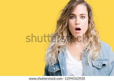 Beautiful young blonde woman wearing denim jacket over isolated background afraid and shocked with surprise expression, fear and excited face.