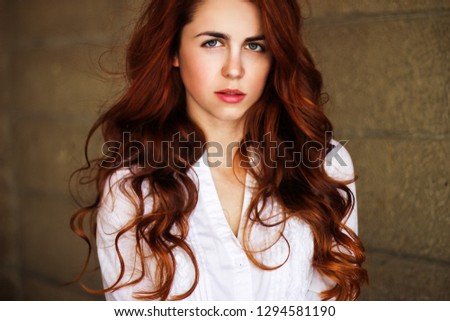 Redhead girl portrait. Beautiful woman with shiny curly long hair in a copper color. Trendy hair colors. Hair colored with henna.