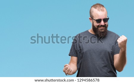Young caucasian hipster man wearing sunglasses over isolated background celebrating surprised and amazed for success with arms raised and open eyes. Winner concept.