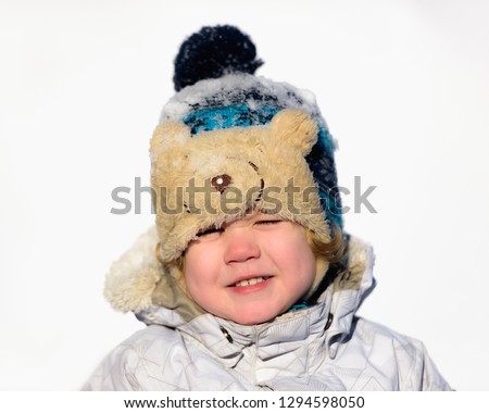  Portrait small child boy having fun wearing a padded jacket and knit hat while playing in the snow.