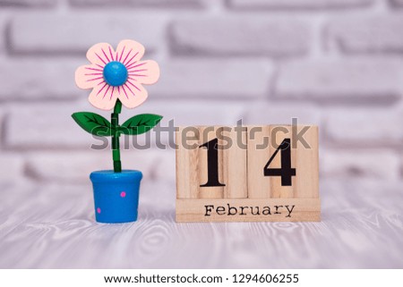 February 14. Day 14 of month on wooden calendar with toy flower on white brick background. Happy Valentines day.