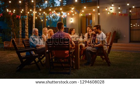 Sitting at the Dinner Table Handsome Young Man Plays the Guitar For a Friends. Family and Friends Listening to Music at the Summer Evening Garden Party Celebration. Royalty-Free Stock Photo #1294608028