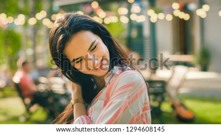 Portrait of Beautiful Brunette with Loose Hair Charmingly Smiling, Straightening Her Hair. In the Background Hot Summer Day and Garden Party in the Backyard.