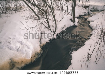 long exposure rocky mountain river in winter with high water stream level and white snow - vintage old film look