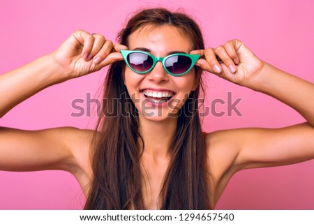 Positive close up portrait of happy pretty brunette woman with long hairs and big smile, wearing vintage 90s trendy sunglasses, pin up style, pink background.
