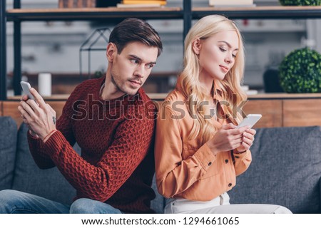 young couple sitting back to back and using smartphones, jealousy concept  Royalty-Free Stock Photo #1294661065
