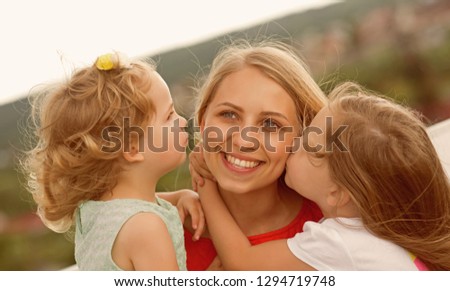 Mothers day concept. Daughters kiss mother on natural landscape. Happy childhood, family, love. Woman and girls sit on bench. Summer vacation, leisure, activity, lifestyle