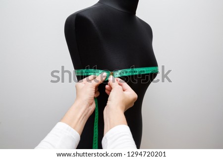 Woman's hands measuring circumference of breast with green measuring tape on black mannequin. Right size. Handmade work. Feminine hobby. Gray background. Closeup. Point of view shot. Royalty-Free Stock Photo #1294720201
