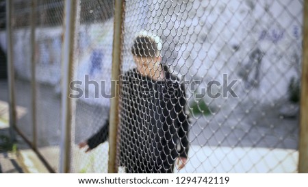 Teen boy behind fence confinement, boarding school restrictions, broken future Royalty-Free Stock Photo #1294742119