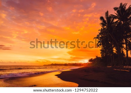 Bright sunset or sunrise with ocean waves and coconut palms in Bali, Keramas