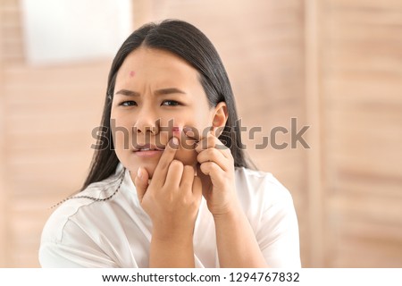 Portrait of young Asian woman with acne problem squishing pimples in bathroom Royalty-Free Stock Photo #1294767832