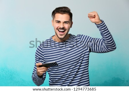 Happy young man after winning game on smartphone against color background