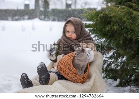 In winter, in the Park a little funny girl of two years sitting in a sleigh and holding a gray kitten. The child is wearing a sheepskin coat, shawl and boots. A very emotional child.