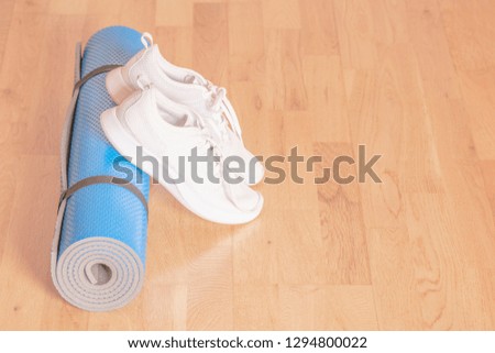 Rolled up blue yoga mat with white sneakers on the floor. Healthy lifestyle concept