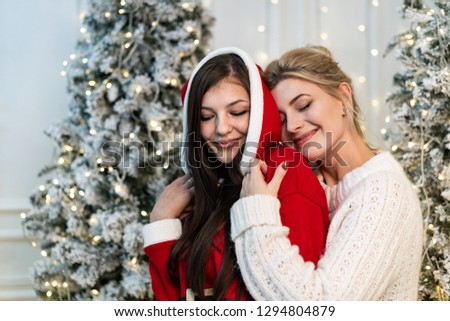 Two beautiful sisters in sweaters hugging near the christmas tree. New Year concept.