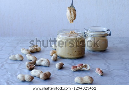 Homemade peanut butter in glass jar with peanuts spread on the table