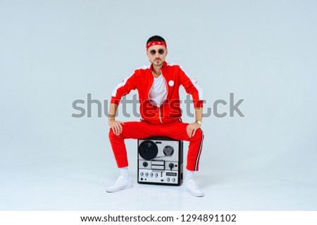 cheerful fashionable man wearing a red sports suit sitting with a retro tape recorder. proud and successful style of the 90's. Royalty-Free Stock Photo #1294891102