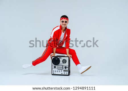 cheerful fashionable man wearing a red sports suit dancing jumps with a retro tape recorder. interesting and fervent style of the 90s. Royalty-Free Stock Photo #1294891111