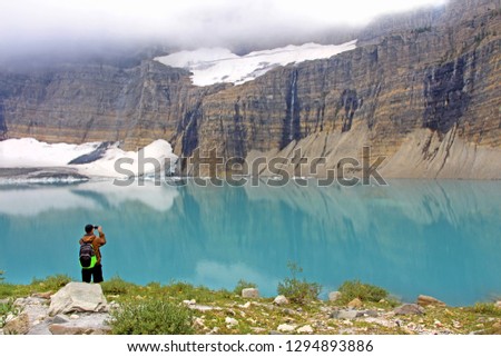 Grinnell Glacier trail in Montana, USA - Man, tourist and hiker is taking picture of beautiful turquoise lake and rocky mountains with glacier.