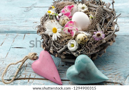 Happy Eastern with Rustic still life - easter eggs in natural bird nest with feathers, white and pink flowers and wooden hearts on an old blue wooden board. Spring, Easter concept. 
