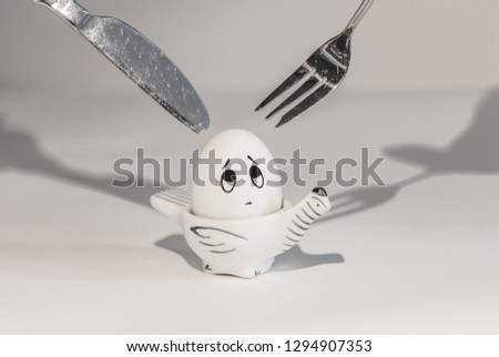 small pretty egg is afraid of a looming fork and knife from above, look up, fear of an egg, sadness in painted eyes