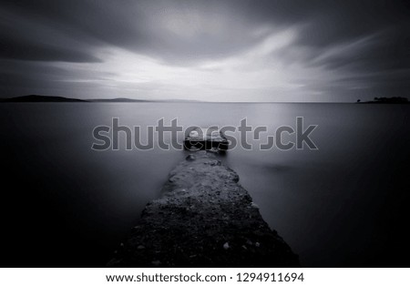 Long exposure of a small abandoned rock jetty (pier) on sea in black and white. Beautiful seascape shot with slow shutter speed was used to see the movement of the clouds in the sky.