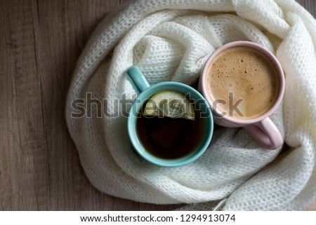 Top view of Cups of hot coffee or cappuccino and hot tea with lemon. Warm scarf a on wooden table. Good morning. Winter mood concept. Warm autumn or winter picture. Time for relax. Coffee vs Tea. Love