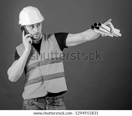 Negotiation concept. Engineer, architect, builder on busy face speaks on smartphone while holds blueprints, copy space. Man, architect in helmet supervises construction on phone, red background.