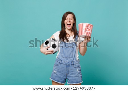 Laughing young girl football fan watching match support favorite team with soccer ball bucket of popcorn isolated on blue turquoise background. People emotions, sport family leisure lifestyle concept