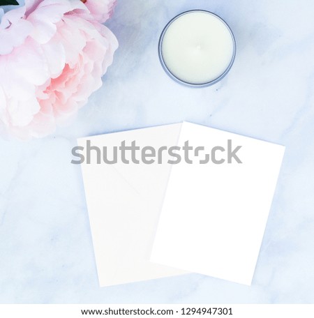 Stationery flat lay background on white marble counter with pink peonies and candle.