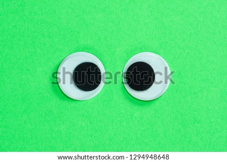 Cross-eyed googly eyes on neon green background, mad funny toys eyes close-up.
