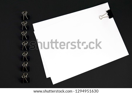 White sheets and binder clip on black background, top view	