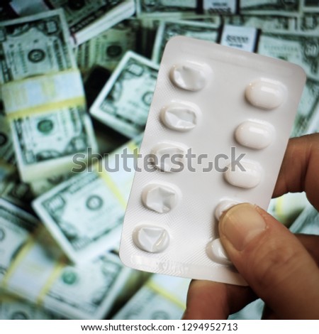 High costs of expensive medication concept. Vertical. Near empty blisters pack of pills in hand on swirly bunch of dollar bills background. Medicine, health insurance,medical costs, prescription icon