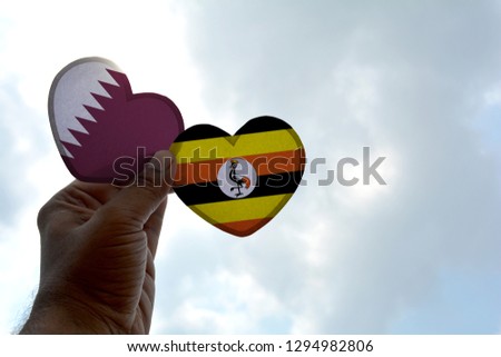 Hand holds a heart Shape Qatar and Uganda flag, love between two countries