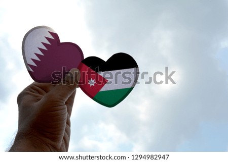 Hand holds a heart Shape Qatar and Jordan flag, love between two countries