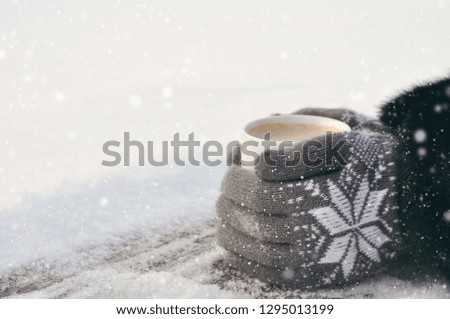 Winter picture: hands in knitted gray gloves holding a Cup of hot coffee on a snowy day on a wooden rustic background in the village. copyspace. top view
