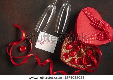 Valentine's Day with a box of chocolates in the form of a heart with a bottle of champagne with glasses and a note. Top view