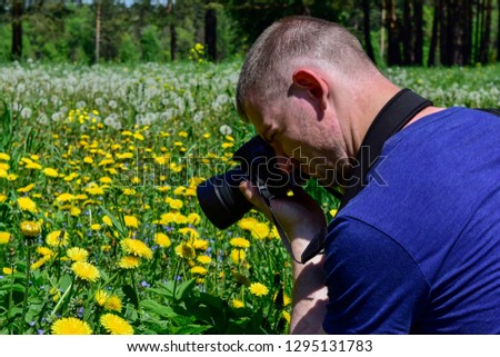 A young man takes photos of yellow flowers on the field. A man holding a camera.