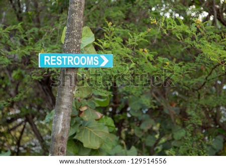 Blue sign pointing way in garden to restrooms or toilets