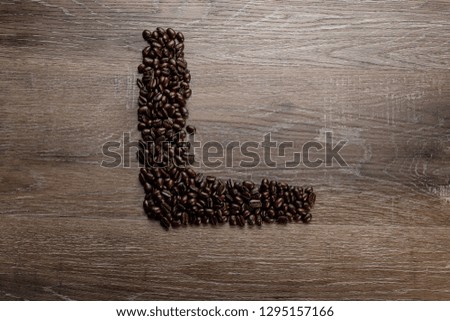 Dark roasted coffee bean arranged on a wooden table in the shape of text alphabet letter L
