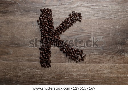 Dark roasted coffee bean arranged on a wooden table in the shape of text alphabet letter K