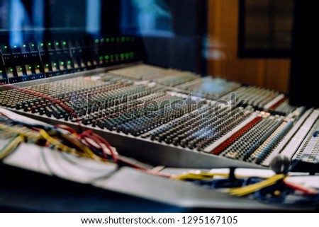 Professional soundboard including audio mixer control panel with buttons and sliders, cords and microphone in recording studio. Focus on soundboard knobs.